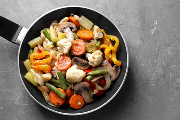Different vegetables and mushrooms in frying pan on grey table, top view