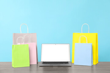 Internet shopping. Laptop and colorful paper bags on wooden table against light blue background