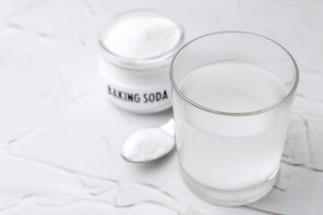 Glass with water and baking soda on white textured table, closeup