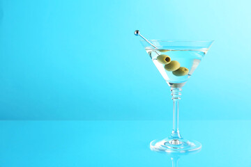 Martini cocktail with olives in glass on light blue background, space for text