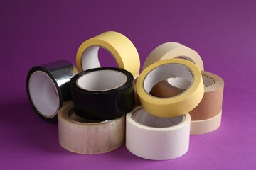 Rolls of different adhesive tapes on purple background