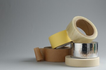 Rolls of different adhesive tapes on grey background, space for text