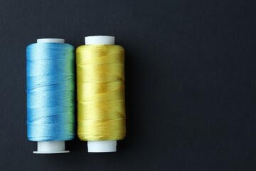 Spools of colorful sewing threads on black background, top view. Space for text