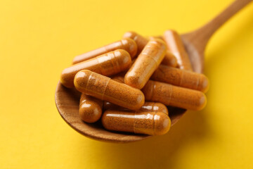 Turmeric capsules in spoon on yellow background, closeup