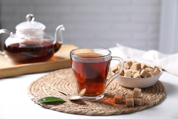 Aromatic black tea in cup and brown sugar cubes on white table