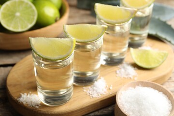 Tequila shots with lime slices, salt and agave leaves on wooden table, closeup