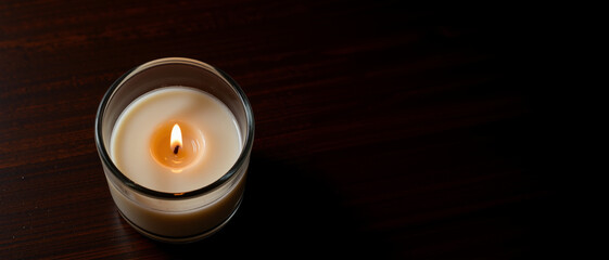 Burning candle in a glass holder exuding a warm glow symbolizing peace and tranquility against a dark wooden background