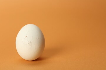 One egg with cracked shell on coral background, closeup. Space for text