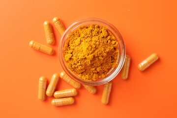 Turmeric powder in bowl and capsules on orange background, flat lay