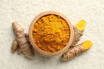 Turmeric powder in bowl and roots on light textured table, flat lay