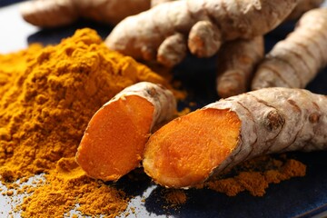 Aromatic turmeric powder and fresh roots on blue plate, closeup