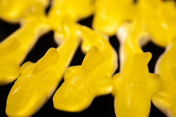 A close-up of several yellow gummy shark candies with a shiny, translucent texture arranged on a...