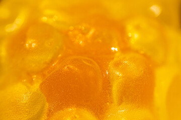 An extreme close-up of a transparent, yellow gummy candy with a bumpy, textured surface resembling...