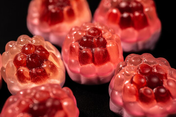 A close-up of transparent raspberry-shaped gummy candies with a shiny, bumpy texture. The bright...