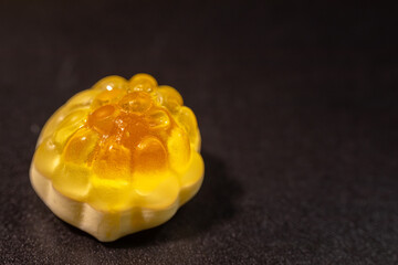 An extreme close-up of a transparent, yellow gummy candy with a bumpy, textured surface resembling...