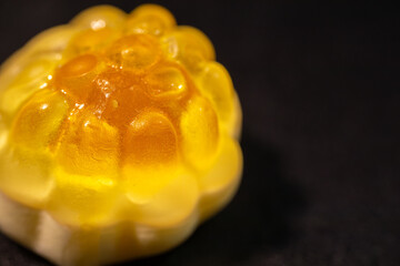 An extreme close-up of a transparent, yellow gummy candy with a bumpy, textured surface resembling...