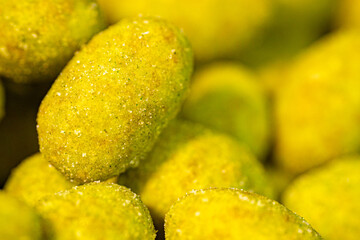 Extreme close-up of green-coated peanuts with a textured layer of seasoning and visible salt crystals. The macro perspective highlights the crunchy coating and rich flavor details.