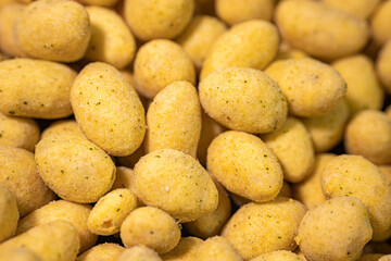 A macro shot of crunchy, spice-coated peanuts with a golden yellow hue. The textured surface highlights their crunchy coating, making them a tasty snack option.
