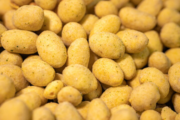 A macro shot of crunchy, spice-coated peanuts with a golden yellow hue. The textured surface highlights their crunchy coating, making them a tasty snack option.