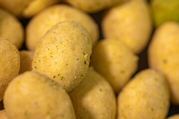 A macro shot of crunchy, spice-coated peanuts with a golden yellow hue. The textured surface highlights their crunchy coating, making them a tasty snack option.