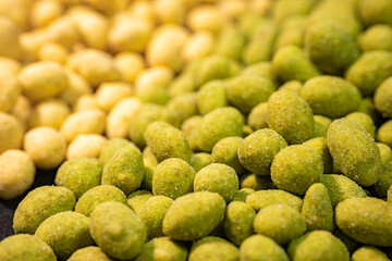 A detailed close-up of two varieties of peanuts, one with a green spice and the other with a yellow coating. The contrasting colors and textures highlight this crunchy snack.