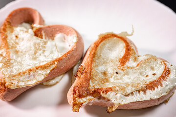A close-up of heart-shaped sausages stuffed with a fried egg on a white plate. The dish has a golden brown crispy texture, making for a creative and delicious breakfast presentation.