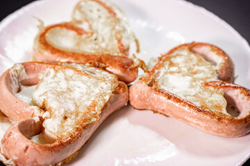A close-up of heart-shaped sausages stuffed with a fried egg on a white plate. The dish has a golden brown crispy texture, making for a creative and delicious breakfast presentation.
