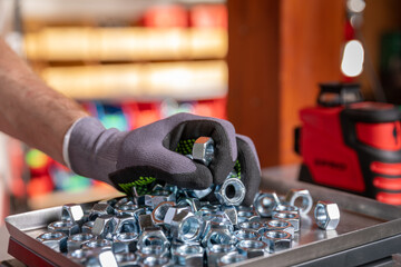 A closeup view of a hand meticulously sorting various metal bolts and nuts in a workshop setting