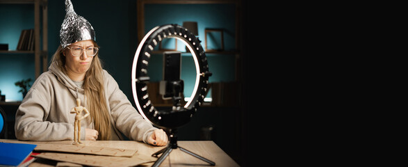 Crazy conspiracy theorist blogger woman in eyeglasses streaming live at home using smartphone and...