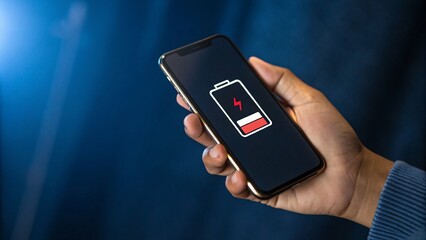 Hand holding a mobile phone with low battery icon representing the urgency for sustainable solutions and smart technology in future business innovation.