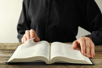 Woman reading Holy Bible in English language at wooden table, closeup