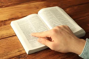 Naklejka premium Man reading Holy Bible in English language at wooden table, closeup