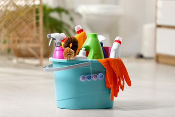 Bucket with different cleaning supplies on floor in bathroom
