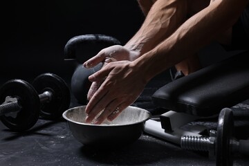 Man applying talcum powder onto his hands above bowl before training in gym, closeup