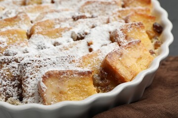 Delicious bread pudding with raisins and powdered sugar on table, closeup