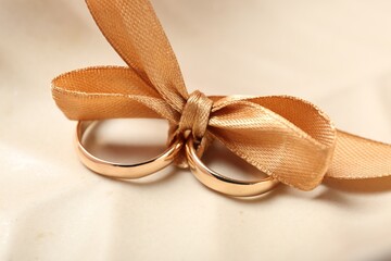 Wedding rings tied with ribbon on beige background, closeup