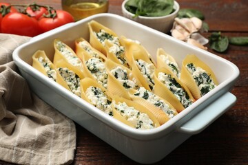 Delicious conchiglie pasta with ricotta cheese and spinach in baking dish on wooden table, closeup