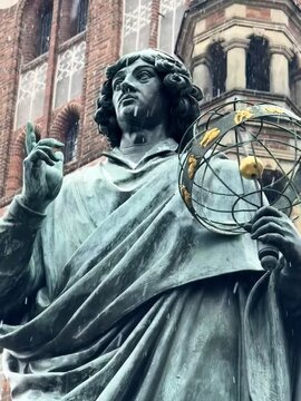 Pomnik Mikołaja Kopernika w zimowej scenerii &ndash; pomnik astronoma w Toruniu. Rynek toruński, zima, padający śnieg.