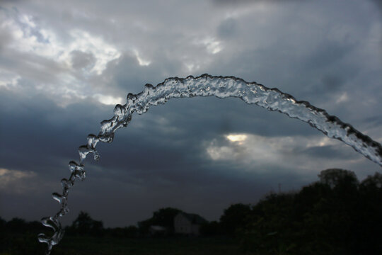 an arched stream of water from a hose against a background of thunderclouds