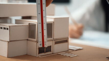Closeup image of skilled professional engineer hand using ruler measures house model on table with...