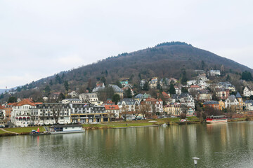 A picturesque view of Heidelberg, Germany, featuring the city’s historic architecture, lush green hills, and the iconic Neckar River. The blend of old and modern elements creates a timeless atmosphere