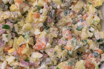 Close-up of a Russian-style potato salad, with mayonnaise, eggs, and ham mixed in, along with fresh vegetables and vibrant colors