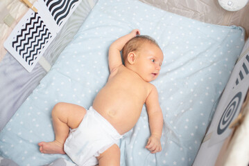 baby boy looking at contrasting black and white pictures, child in diaper lying in bed or playpen.