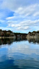 Fototapeta premium Vertical photo of Zalew Zakrzowek with rocks and sky reflected in blue water. Ideal for nature, travel, outdoor, and scenic landscape themes. Perfect for peaceful and serene visuals.