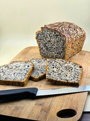 Photo showing freshly baked bread on a wooden board, partially sliced, with a knife lying nearby.