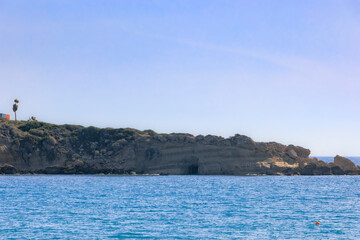 Naklejka premium Rocky coastal cliffs with a sea cave under clear blue sky, Paphos, Cyprus, 23.11.2024