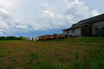 Obraz premium A view of a small farm located next to a vast field, meadow or pastureland with numerous hay bales visible, together with various farming equipment like tractors and ploughs seen in Poland