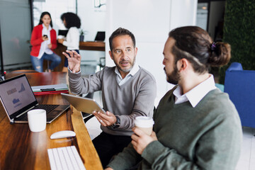 Latin senior man manager and young man employee working together on computer at creative office in Mexico Latin America, hispanic teamwork