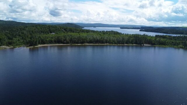 Panoramic aerial view of the large freshwater lake with its sandy beaches constituting its forest shore under a cloudy sky. Lake Matapedia, Quebec,Canada.