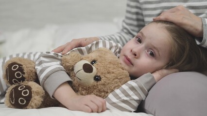 little child daughter lies her mother lap hugging teddy bear. time sleep kid. mom strokes cares girl daughter head. nice relaxation before bed. childhood dream arm mother. happy family life together